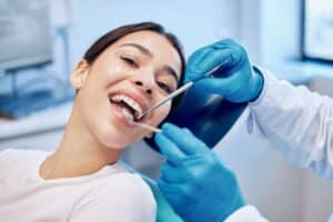 Woman smiling in dentist chair as dentist examines her smile during checkup